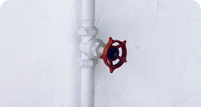 White water pipe with red valve handle mounted on a white wall.