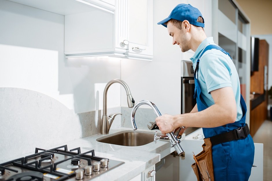 Plumber installing a new kitchen faucet in a modern home kitchen.