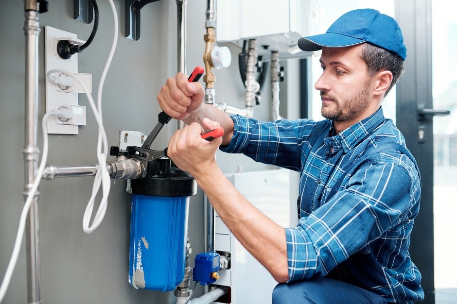 Plumber installing or repairing a water filtration system using tools.